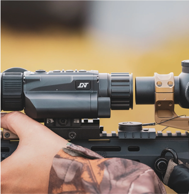 Close-up of a night vision device mounted on a rifle hand adjusting controls.