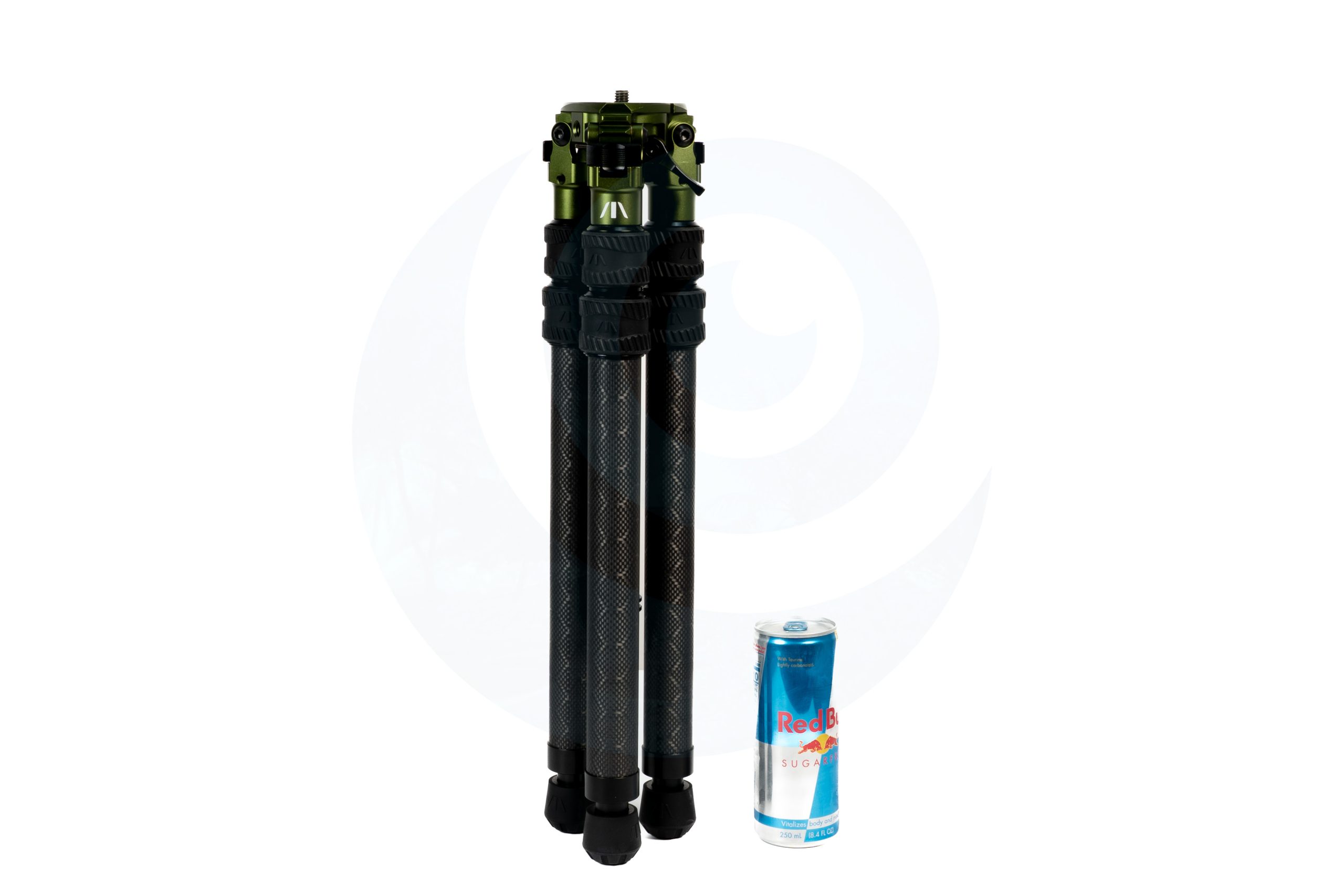 Folded tripod with green metal head next to a can of Red Bull on a white background.